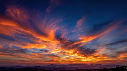 Naklejka premium Dramatic orange and blue sunrise lights up a layered mountain landscape with beautiful cloud formations in the sky