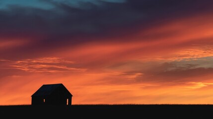 Silhouette of a rustic barn against a dramatic orange and purple sunset sky creating a peaceful rural countryside scene