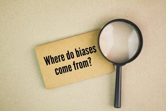 magnifying glass and paper with the question words Where do biases come from?