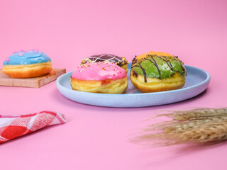 Colorful assorted donuts with icing and sprinkles on pastel pink background