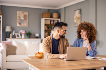 Diverse Professional Couple Collaborating On Project At Wooden Table In Contemporary Home Office Space With Natural Light