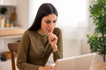 Brunette Woman in Green Sweater Using Laptop at Wooden Table in Bright Modern Home