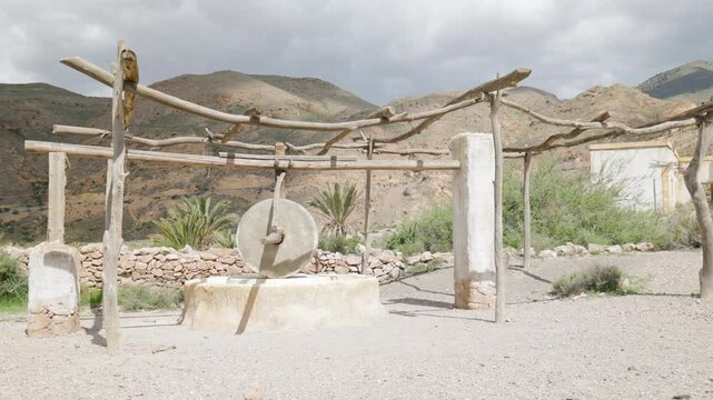 Old Stone Mill Structure in Tabernas Desert, Almeria, Spain &ndash; Rustic Grinding Wheel and Wooden Framework in Arid Mountain Landscape Under Cloudy Sky