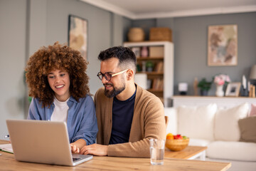 Smiling Couple Works Together on Laptop at Wooden Table in a Cozy Modern Home