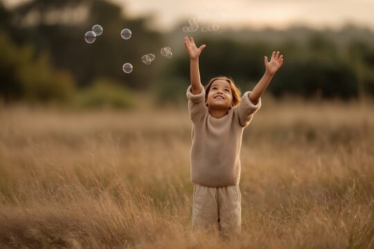 A child joyfully reaches for floating bubbles in a golden field, creating a whimsical and carefree moment of childhood delight.