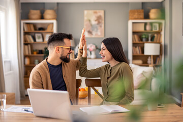 Joyful Coworkers Share High Five Moment At Wooden Desk With Laptop In Cozy Home Library Setting