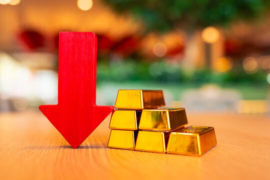 Gold bars and red arrow pointing down placed on the table, concept of gold price is decreasing due to going up high.