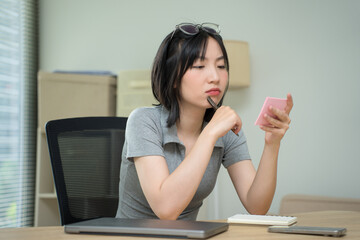 Young Asian person engaged in deep thought while looking at a notepad during an office work session...