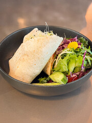 Side view of healthy vegan wraps with vegetables in a dark grey bowl on a light grey table