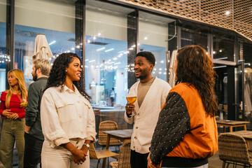Cheerful multi ethnic friends laughing and sharing drinks while enjoying lively conversations at a vibrant evening party