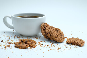 A white ceramic cup of black coffee placed beside stacks of crunchy chocolate chip cookies, with natural touch scattered crumbs. Perfect use in advertising, breakfast, packaging, or cozy moments