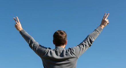 Man raising arms signifying victory and achievement against clear blue sky, showing positive emotion