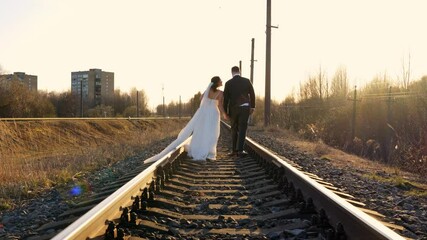 Husband and wife on life journey - walking on train tracks during sunset, back view