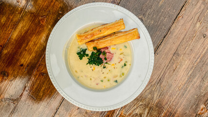 A close-up view of a delicious soup bowl garnished with herbs and accompanied by a crispy breadstick on a wooden table.