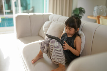 Child girl playing a game on tablet and sitting on sofa 
