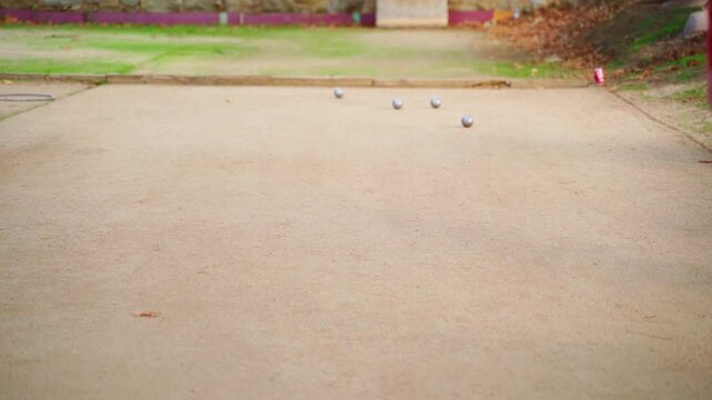 Professional player throwing metal boules balls on sandy field, showcasing precision skill during outdoor leisure activity in slow motion sequence