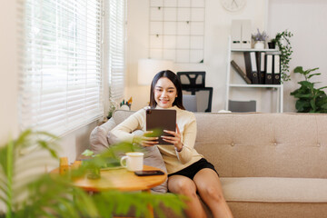Attractive woman, freelancer holding and using digital tablet, sitting at cozy sofa in living room....
