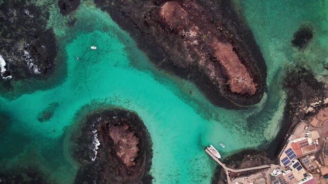 Bird's eye view of turquoise and crystal clear waters, rocky coastlines, and volcanic terrain by 4k aerial drone view of Puertito Isla de Lobos, Fuerteventura