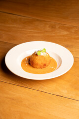 Pumpkin and corn arancini—Italian rice balls coated with breadcrumbs and deep-fried—served with tomatina sauce on a white plate, placed on a brown table in a restaurant setting.