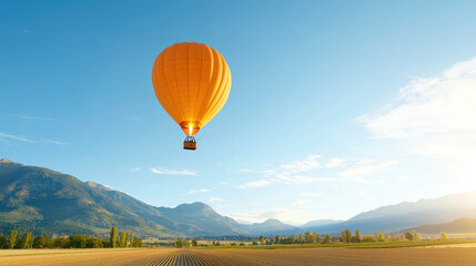 Obraz premium Vibrant orange hot air balloon floats gracefully over picturesque landscape, showcasing mountains and fields under clear blue sky