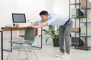 Handsome man exercising with chair in office