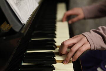 Obraz premium Child or teen hands playing on a classic acoustic piano. Close-up of fingers on the keys, with sheet music visible in the background. The soft lighting and focus on hand movement create an atmosphere 