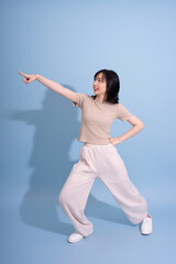 Young Asian woman posing energetically against a blue background while pointing and smiling during a casual photoshoot