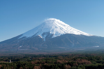 Panoramic view of active stratovolcano Mt. Fuji with snow covered symmetrical cone and green vegetation in foreground and white clouded blue sky