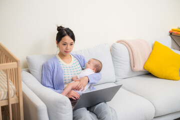 Mother working from home using laptop while caring for baby