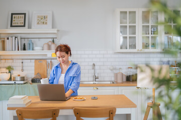 A casual relax young woman is looking at a laptop in the kitchen at home Smiling young female...