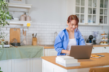 A casual relax young woman is looking at a laptop in the kitchen at home Smiling young female...