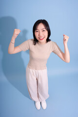 Joyful woman celebrating success with raised fists against a light blue background in a studio...