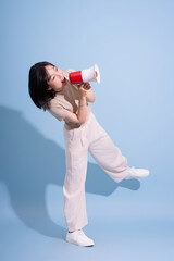 Young Asian woman enthusiastically holding a megaphone in a playful pose against a pastel blue...