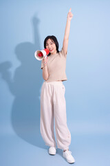 Young Asian woman enthusiastically gestures while holding a megaphone against a blue background...