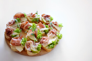 canapes with bacon, pear, herbs and bread are on a wooden plate. close up