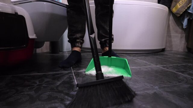 Sweep loose white powder off a tiled floor with a broom. Remove dirt with a broom into a dustpan. Slow motion