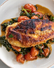 Close-up photo of delicious cooked chicken breast served with spinach and cherry tomatoes. A clean, balanced, and healthy dinner