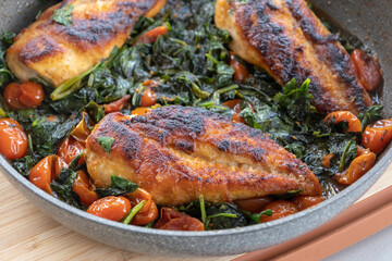 delicious cooked chicken breast with spinach and cherry tomatoes in a pan
