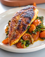 Close-up photo of delicious cooked chicken breast served with spinach and cherry tomatoes. A clean, balanced, and healthy dinner