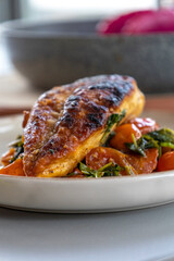Close-up photo of delicious cooked chicken breast served with spinach and cherry tomatoes. A clean, balanced, and healthy dinner