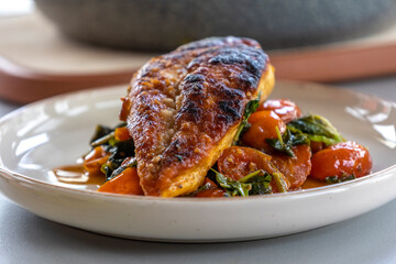 Close-up photo of delicious cooked chicken breast served with spinach and cherry tomatoes. A clean, balanced, and healthy dinner