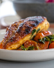 Close-up photo of delicious cooked chicken breast served with spinach and cherry tomatoes. A clean, balanced, and healthy dinner