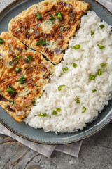Indian omelette with coconut cream, onion, ginger, green chilli and curry leaves served with rice close-up in a plate on a table. Vertical top view from above