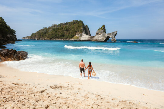 White man and young asian woman walking at the beach, Nusa Penida island, Bali, Indonesia