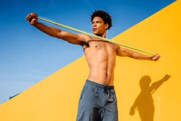 Young man strengthening his upper body outdoors with a resistance band under clear blue skies