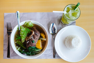 Filipino beef bulalo soup with bone marrow, cabbage, corn, and greens, served with white rice and cucumber juice on the side.