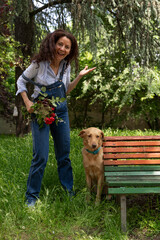 beautiful smiling middle-aged woman with red hair playing with her dog sitting near a metal bench outdoors
