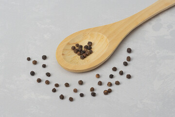 Black peppercorns on a wooden spoon and on a gray background. Dry spicy seasoning for ready meals
