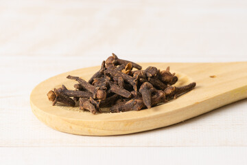 Dried cloves in wooden spoon on wooden light brown background