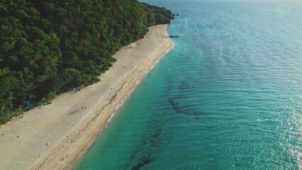 Capturing aerial drone footage of a tropical beach merging with turquoise waters on a sunny day,...